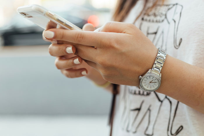 Person holding a smartphone, focusing on security measures while wearing a watch and an elephant-patterned shirt.
