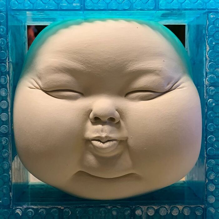 Close-up of a sculpted face blending realism and surrealism, framed by a blue border.