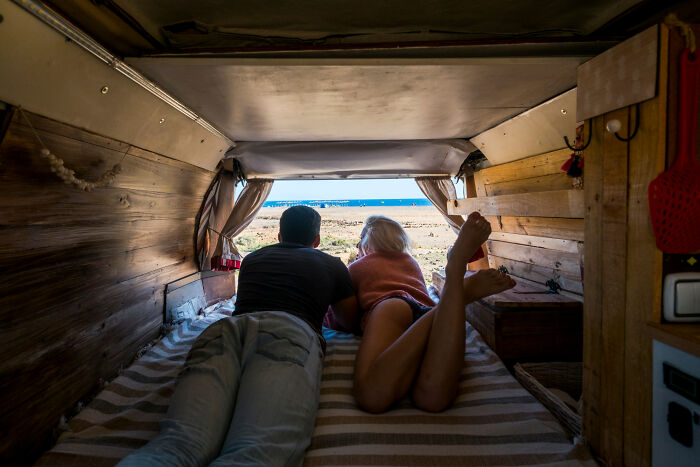 Couple in a van overlooking the ocean, idealizing van life that is often romanticized but can be challenging.