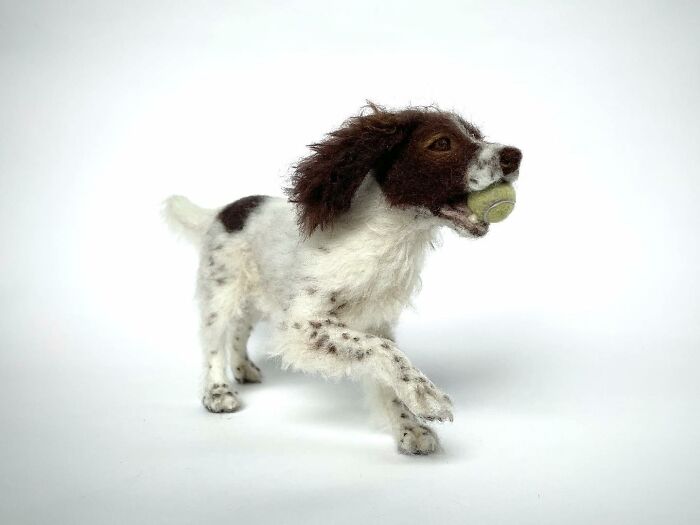 Needle-felted dog sculpture playfully holding a ball, showcasing artistic craftsmanship.
