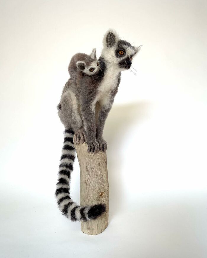 Needle-felted lemur pair perched on a log, showcasing artist's skill in crafting intricate animal sculptures.