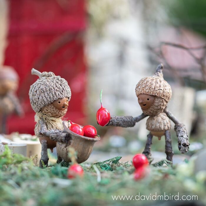 Becorns made from acorns and sticks, one handing a berry to another in a whimsical outdoor setting.