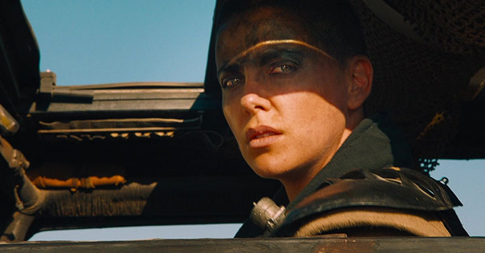 Heroic woman gazes intensely from vehicle, embodying strong female protagonist.