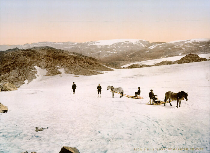 Early color photo of people with horses and sledges on snowy mountains, showing world's appearance 100 years ago.