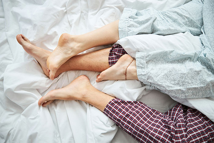 Feet entangled under sheets, symbolizing a cheating girlfriend scenario.