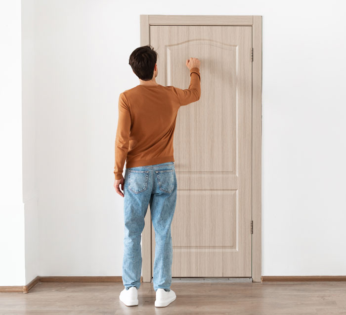 Man in jeans and brown sweater knocking on a closed wooden door. Man in jeans and brown sweater knocking on a closed wooden door.