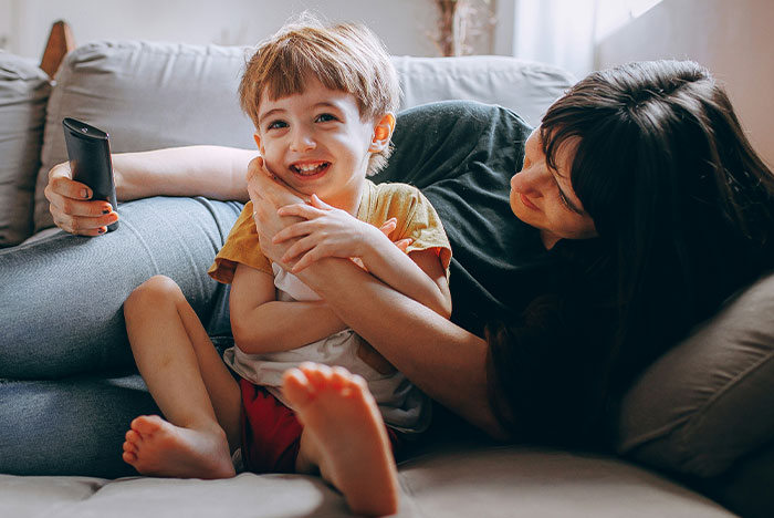 A woman comforts a smiling toddler with a remote, highlighting themes of toddler concussion care.