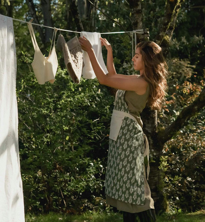 Woman hangs laundry outside in a forest setting amidst neighborhood tensions over chakra alignment practices.