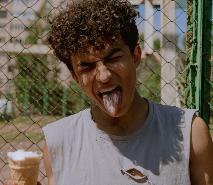 Person wearing a ripped shirt, showing dislike with a blue tongue, holding an ice cream cone, highlighting fashion trends.