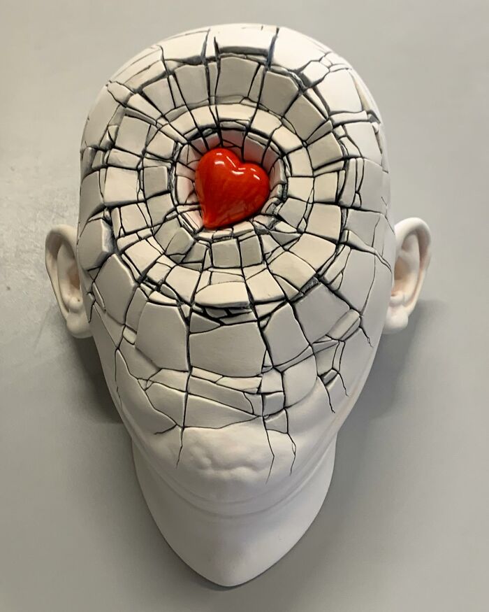 Sculpture blending realism and surrealism: a c*****d head with a red heart at the center.