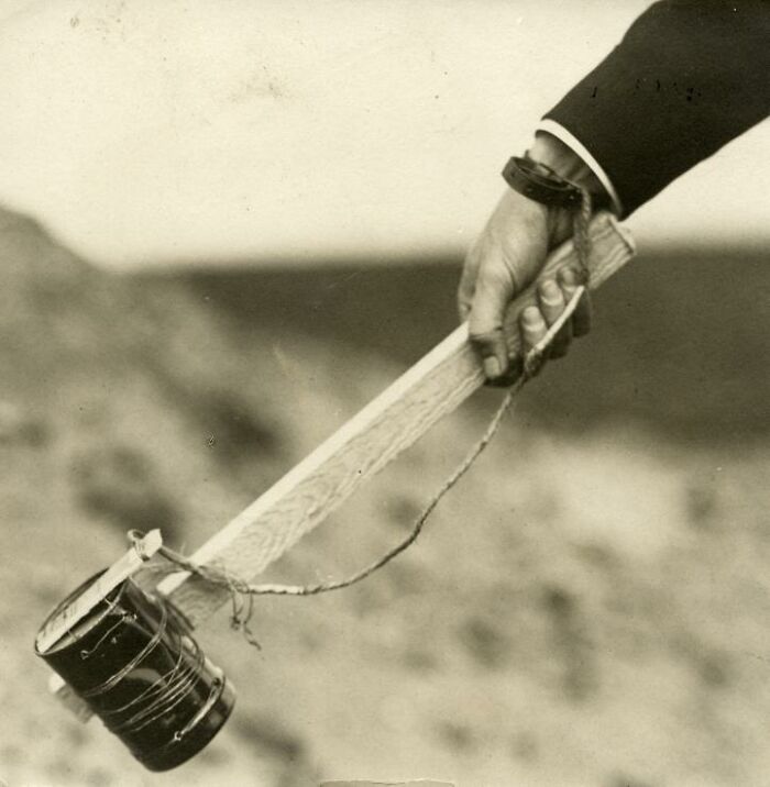 A hand holding a strange invention with a long handle and attached can, showing unique design creativity.