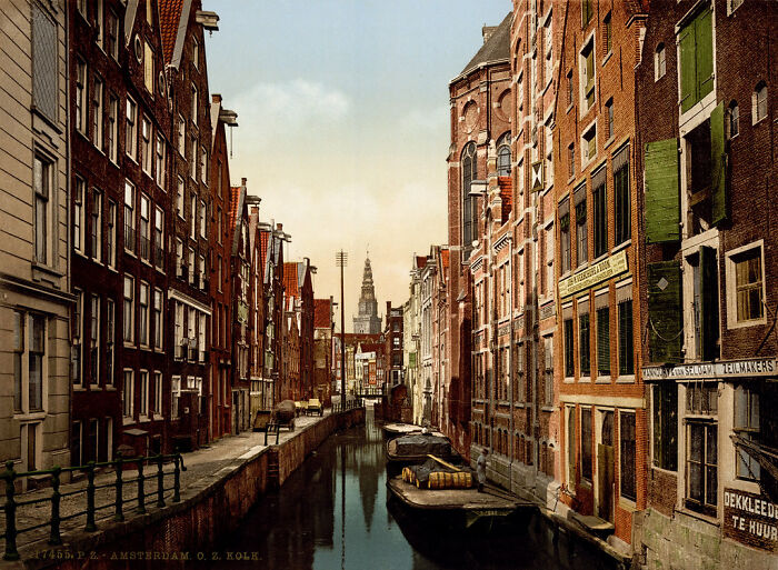 Historic color photo of an Amsterdam canal, capturing early 1900s architecture and reflections in the water.