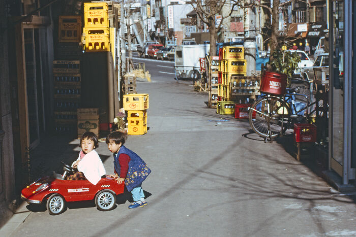 Children playing with a toy car on a busy street in 1973.