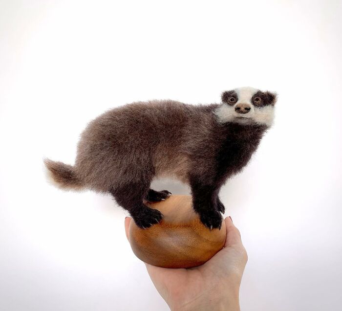 Needle-felted badger sculpture held on a wooden base, showcasing the artist's animal craftsmanship.