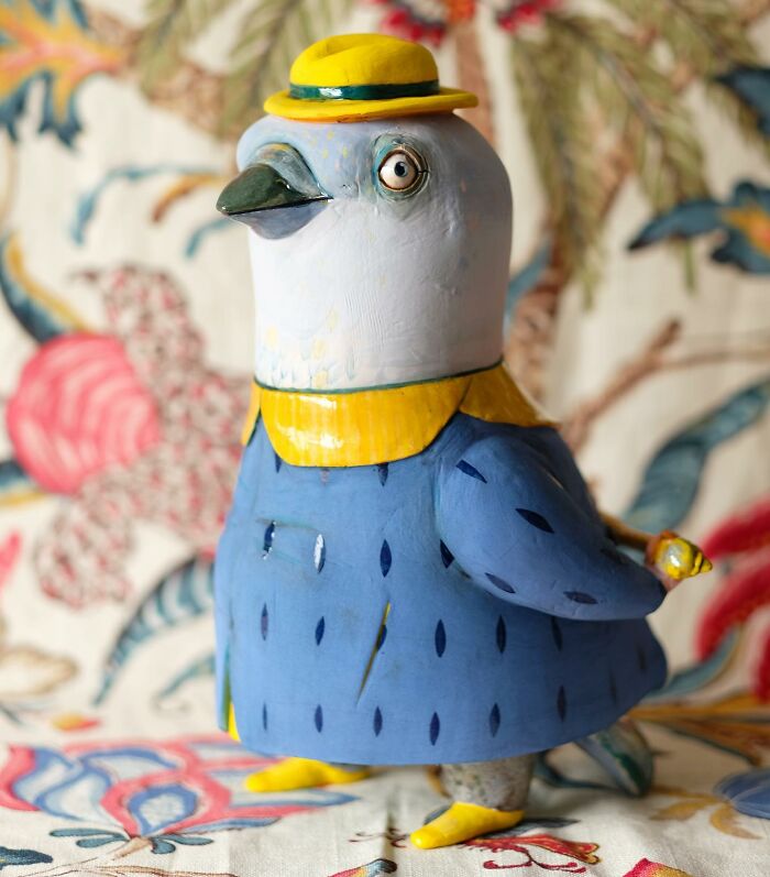 Playful ceramic sculpture of a pigeon in a blue suit with a yellow hat.