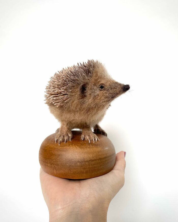 Needle-felted hedgehog sculpture perched on a wooden base, held in hand.