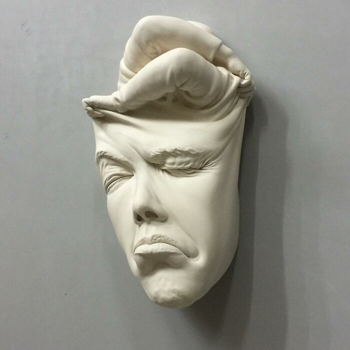 Surrealist sculpture of a face being pressed by a hand, blending realism and surrealism in expressive art.
