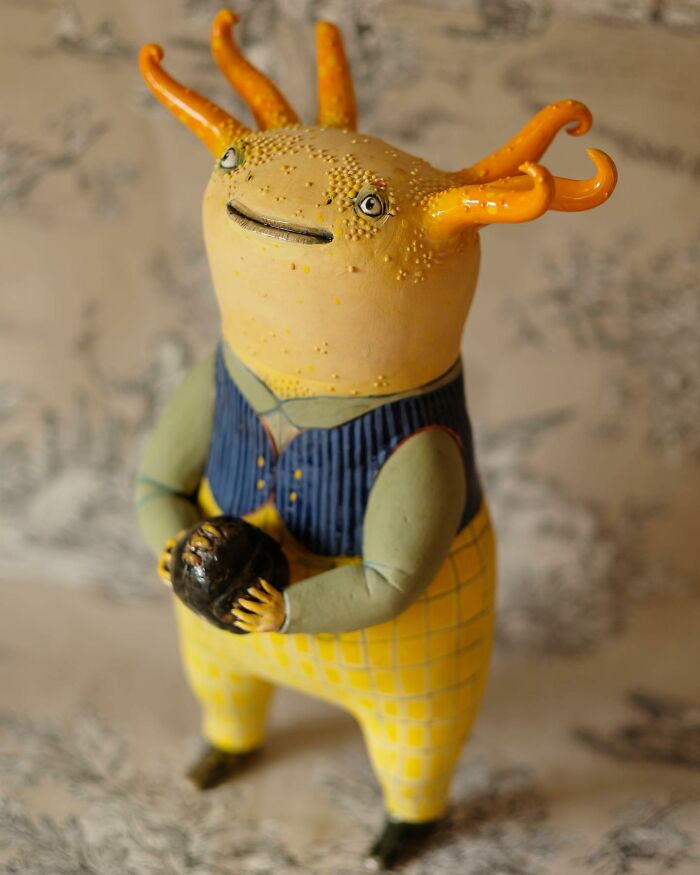 Playful ceramic sculpture by Nastia Calaca featuring a whimsical creature with yellow and orange details.