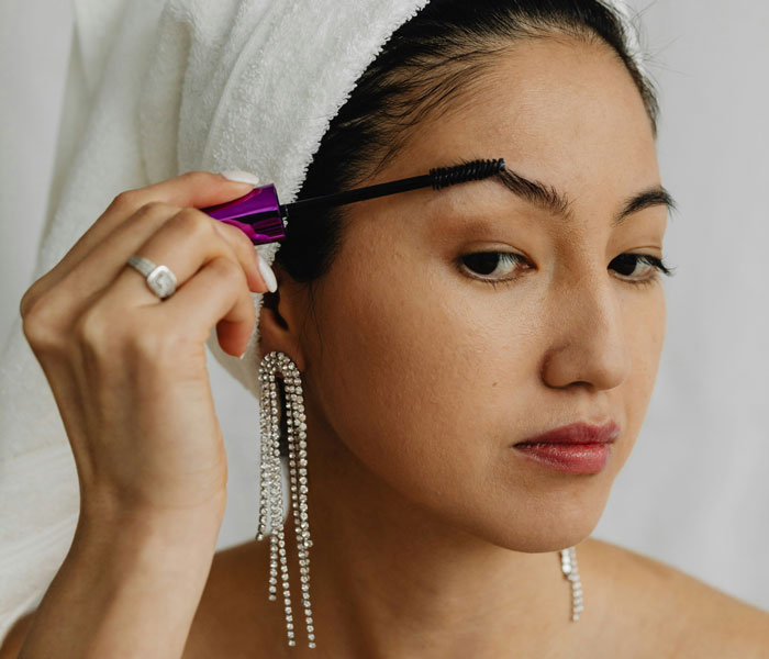 Woman with a towel on her head applies mascara, expressing personal fashion trends dislikes.