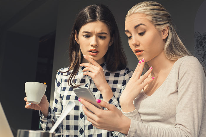 Two women looking concerned at a phone, discussing trading services and financial demands. Two women looking concerned at a phone, discussing trading services and financial demands.