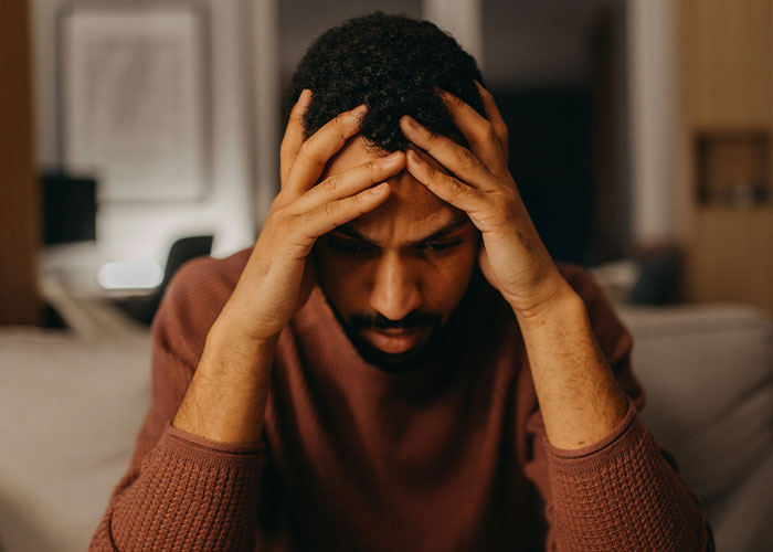 Man sitting on a couch with head in hands, appearing regretful.
