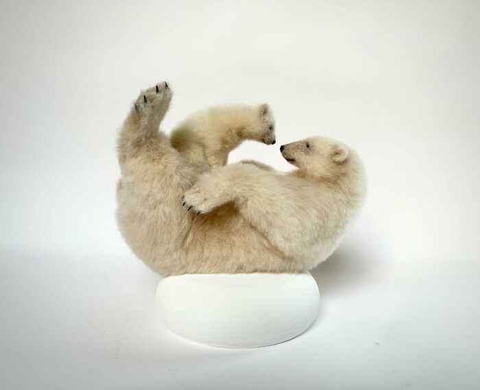 Needle-felted polar bear, artistically crafted, depicting a playful pose on a white base.