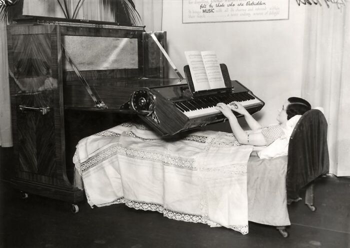 Woman in bed playing a strange invention: a modified vertical piano.