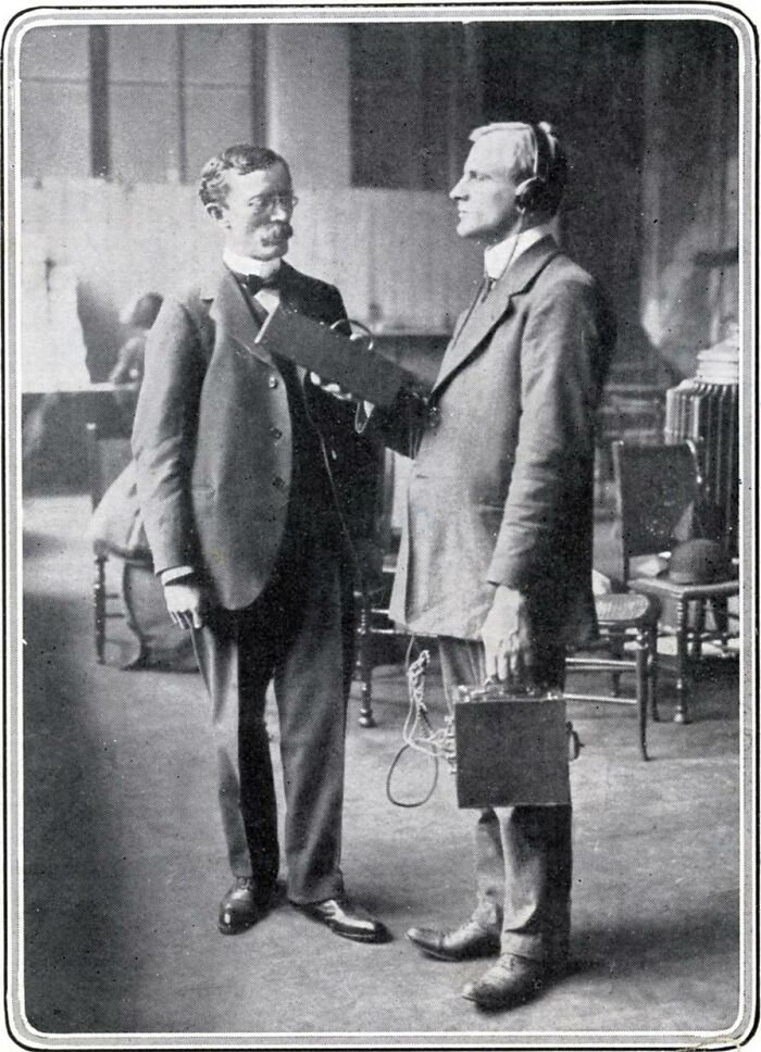 Two men demonstrate a strange invention, possibly an early communication device, in a vintage setting.