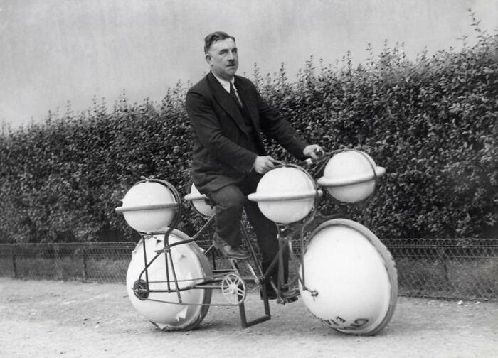 Man riding an unusual bike with large spherical wheels, representing strange inventions.