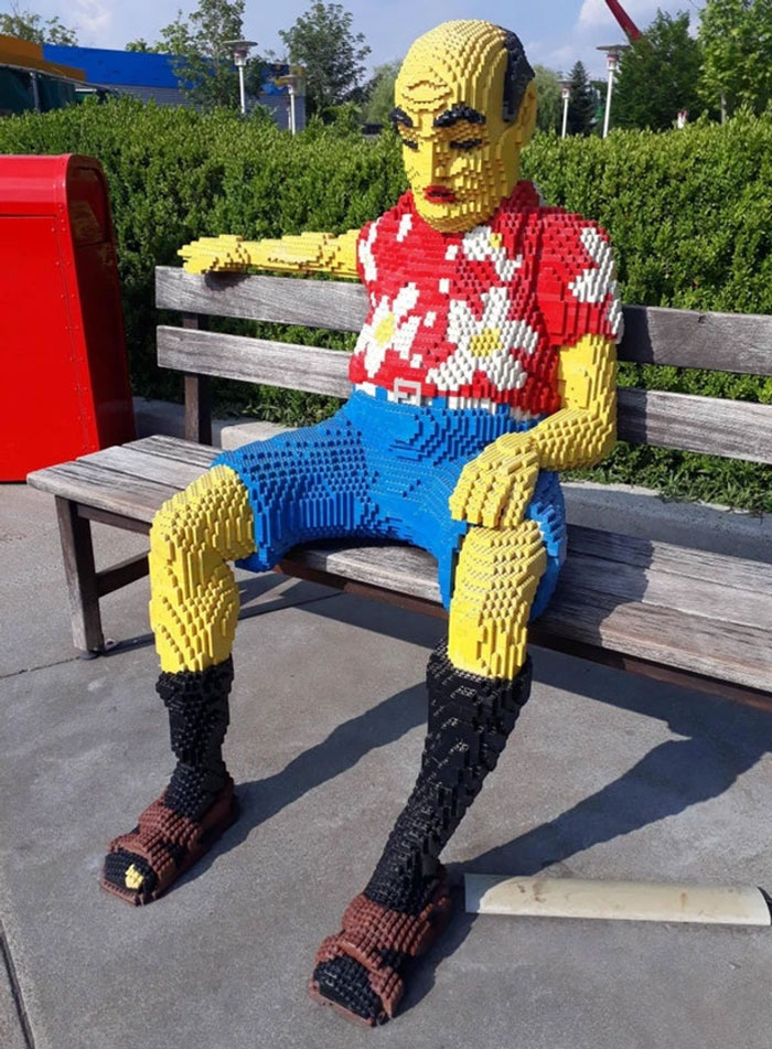 A LEGO figure with a red shirt sits on a park bench, showcasing cool LEGO builds in an outdoor setting.