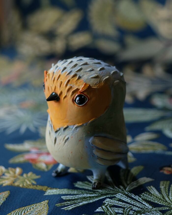 Playful ceramic sculpture of a bird with vibrant colors by Nastia Calaca, showcased on a patterned fabric background.