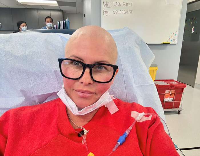 Nicole Eggert in hospital, wearing glasses and a red sweater.