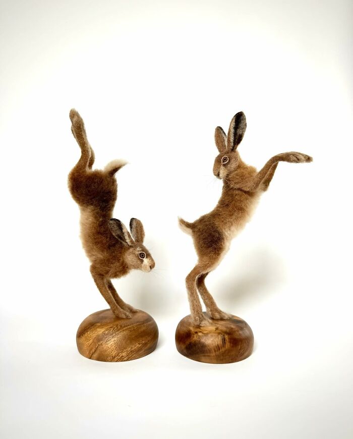Needle-felted animals: two playful hares balanced on wooden bases, showcasing intricate craftsmanship by an artist.