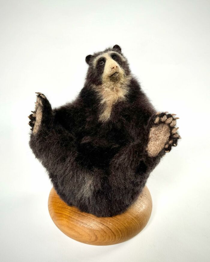 Needle-felted bear sculpture with detailed expression, seated playfully on a wooden base.