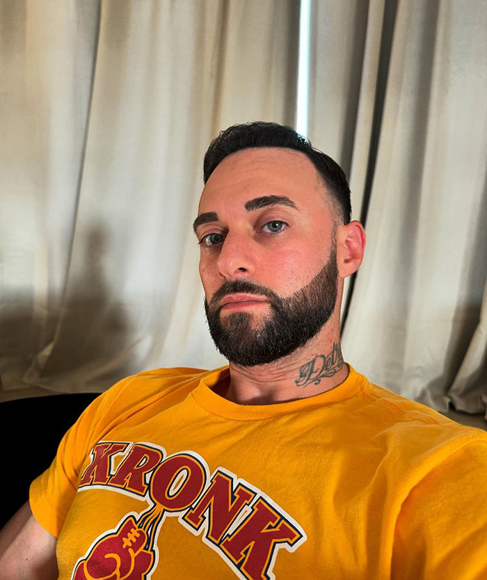 Man in a yellow shirt sitting indoors, appearing thoughtful.