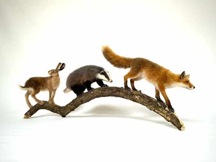 Needle-felted animals: a rabbit, badger, and fox on a curved branch.