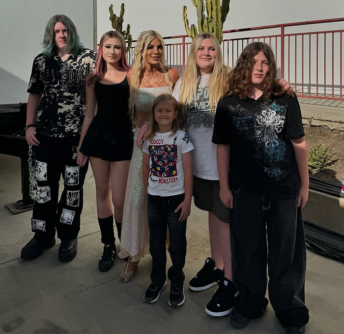 Tori Spelling with family posing together outside with a cactus backdrop during daytime.