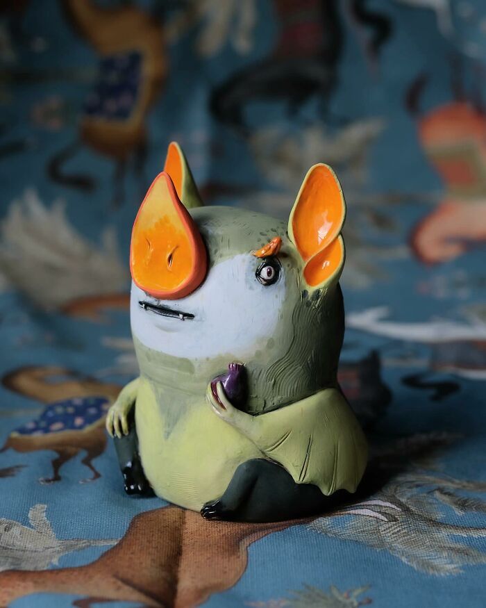 Playful ceramic sculpture by Nastia Calaca, featuring a whimsical creature with vibrant orange ears and a quirky expression.