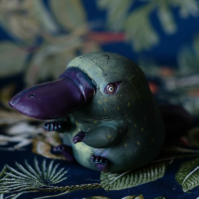 Playful ceramic sculpture of a whimsical creature by Nastia Calaca, featuring a green body and a large purple beak.