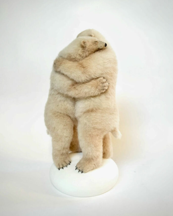 Needle-felted polar bears embracing on a white base, showcasing artist's intricate animal sculptures.