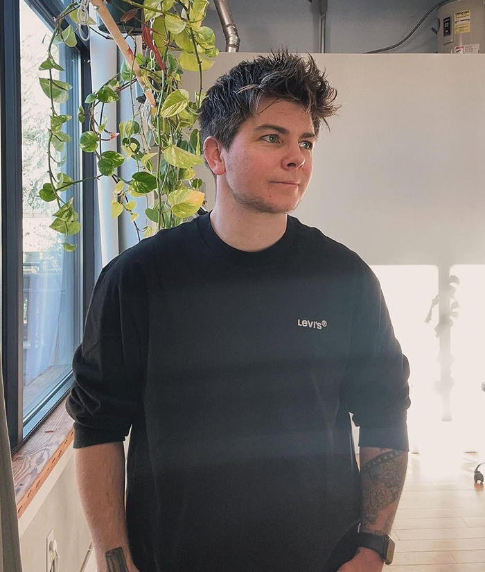 Jules Heron in a salon with short hair, standing near a window.