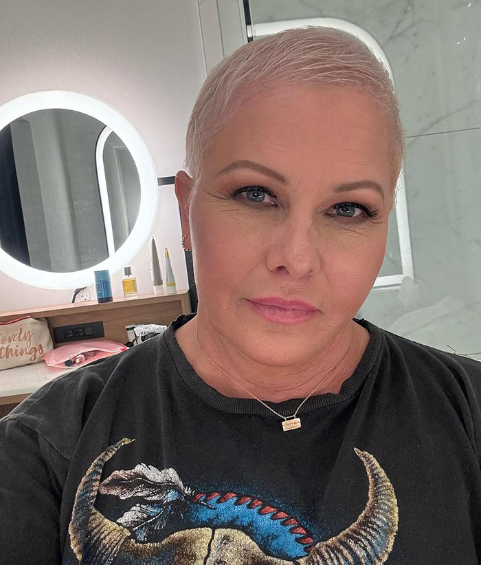 Nicole Eggert with short hair in a serene setting.