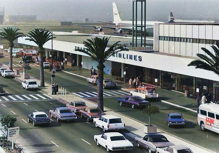 1970s West Coast vintage airport scene with classic cars and TWA airplane in the background.