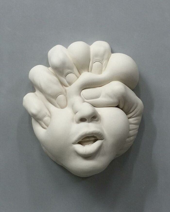 Surrealist sculpture of a face being squeezed by large hands, blending realism and surrealism.