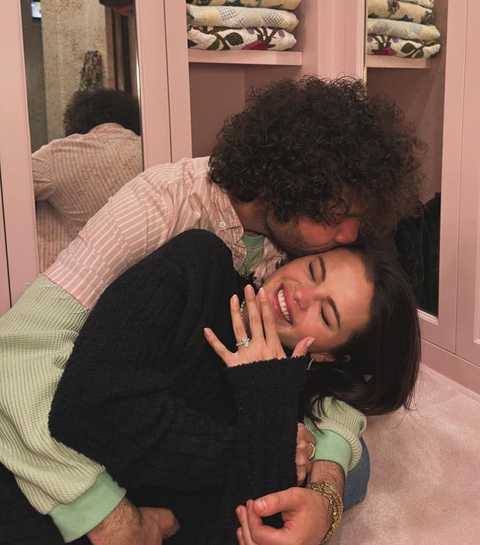 Selena Gomez with engagement ring, embraced by Benny Blanco in cozy setting. 