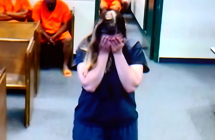 Briana Boston in court covers her face, dressed in dark blue, with people in orange uniforms in the background. Briana Boston in court covers her face, dressed in dark blue, with people in orange uniforms in the background.