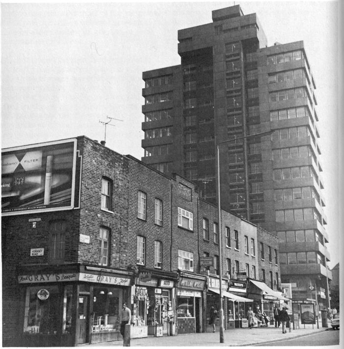 1973 street scene with shops and a tall building, capturing everyday life and architecture from that era.