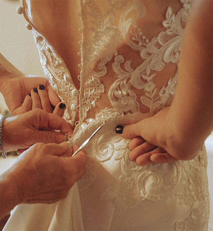 Bride adjusting intricate lace wedding dress before the ceremony, focusing on dress details.