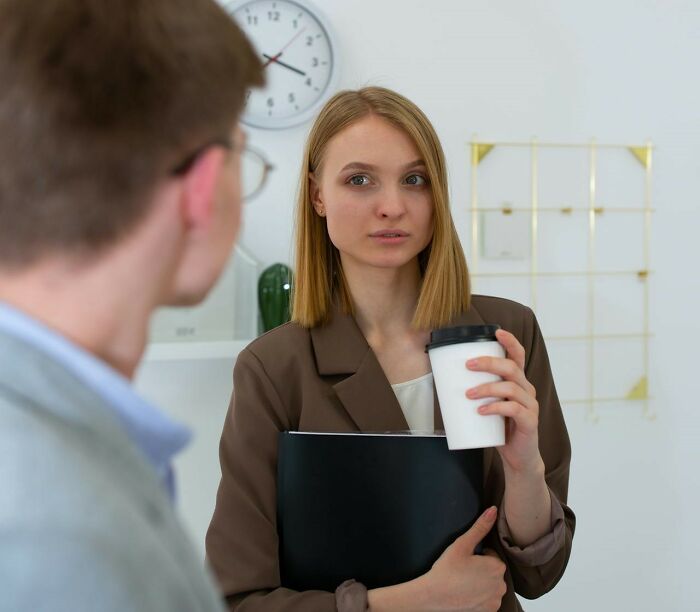 Woman holding coffee cup and folder, talking to a man, illustrating "nice guy" interaction.