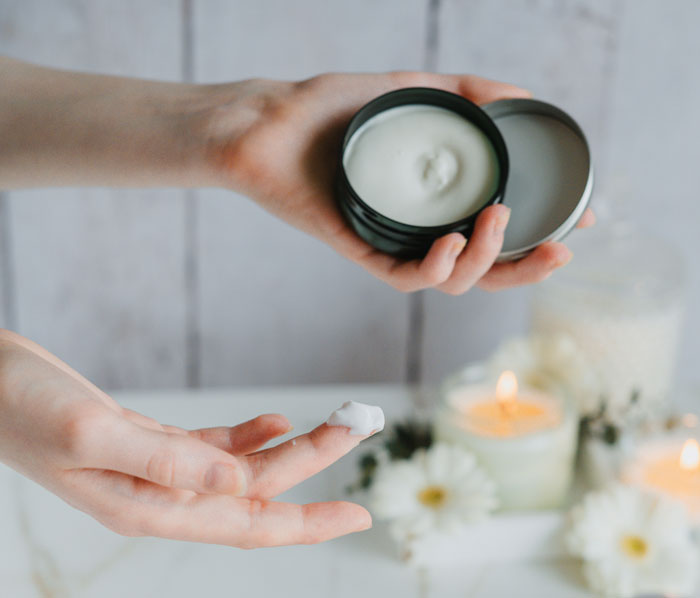 Applying cream with lit candles and flowers in the background, focusing on personal care.